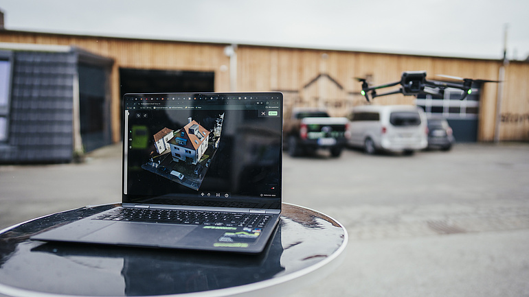 Ein Laptwo auf demvon oben ein Hausdach zu sehen ist und daneben eine Drohne