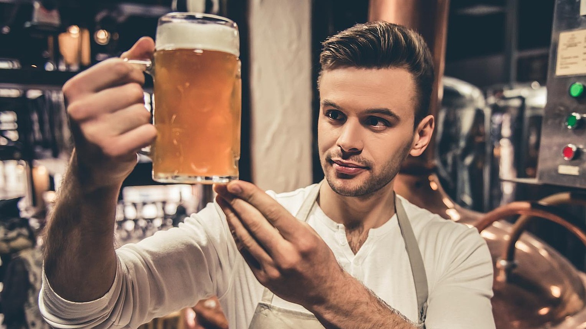 Ein junger Brauer betrachet ein gerade gezapftes Bier in einem großen Glas.