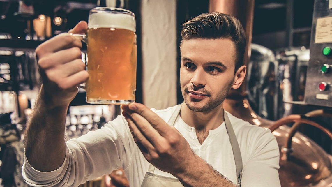 Ein junger Brauer betrachet ein gerade gezapftes Bier in einem großen Glas.