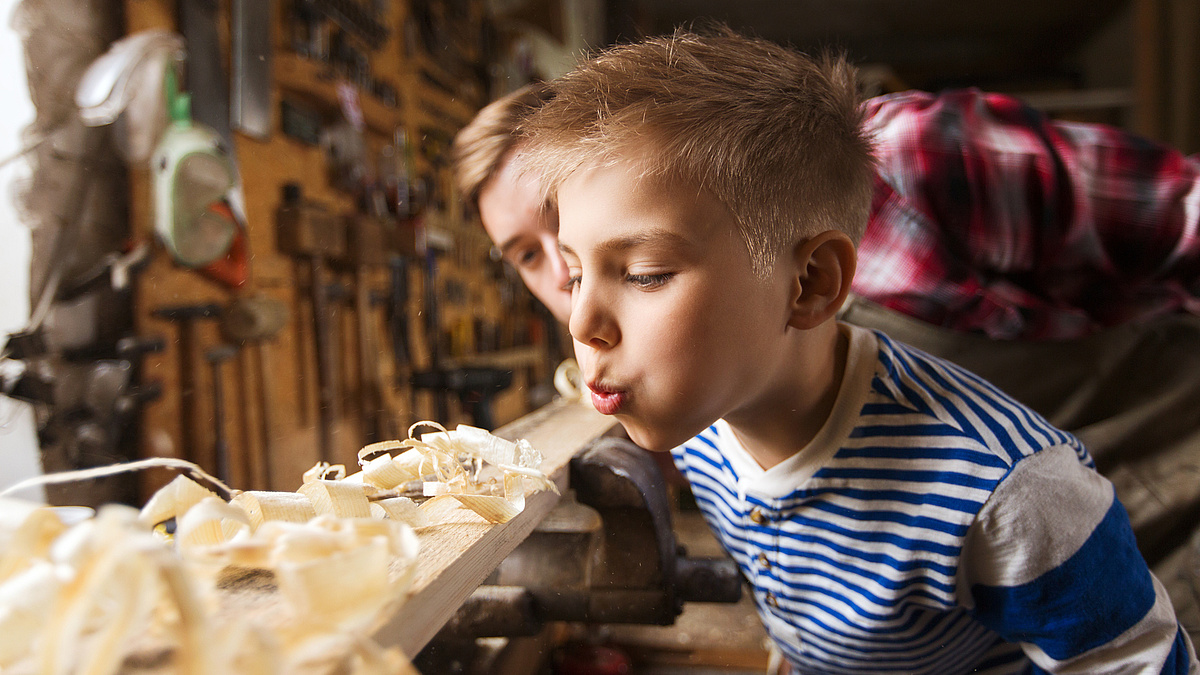 father and little son with wood plank at workshop